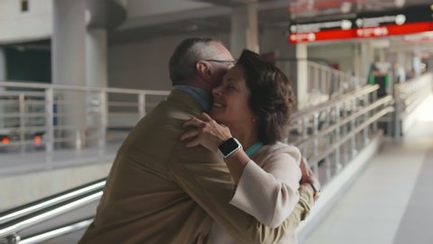 Portrait of lovely mature couple reunion in airport terminal. Senior man meeting his wife at railway station after business trip. Partners happily hugging. Aged couple meeting in airport
