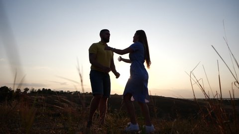 Young beautiful girl runs up to her boyfriend and hugs him. Happy couple kisses against the backdrop of the bright sunset in the evening, slow motion. The guy circles the girl. Unusual romantic date.