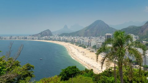 Aerial Timelapse of Copacabana beach in Rio de Janeiro, Brazil. View of the city skyline and buildings, the ocean, traffic and people. Trees in foreground.