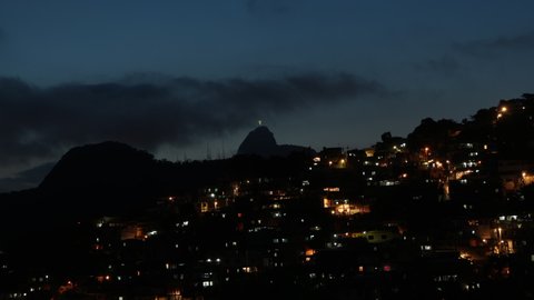 Night Aerial timelapse of Babilonia favela shanty town in Copacabana, Rio de Janeiro, Brazil. Sunrise view of the hill with houses and lights.  Morro and mountain in the background.