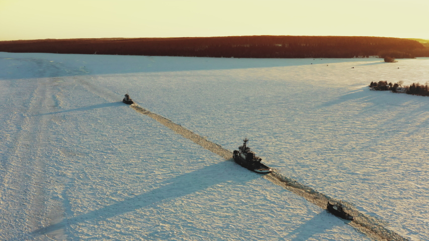 Tugboats break a path through the ice while towing a boat needing repair