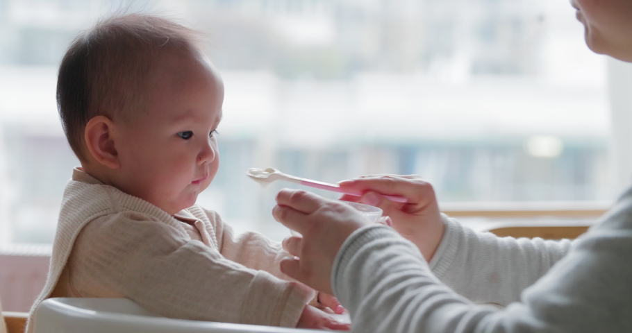 Side view asian mother feeding her baby daughter 9 month Chinese infant girl eating with spoon | Shutterstock HD Video #1045071358