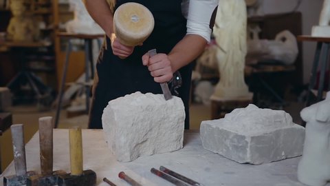 Slow motion of attractive man's hands which holding chisel and hammer and beating on limestone in workshop