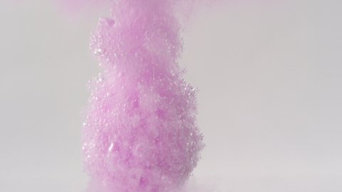 Underwater view of pink bath bomb falling down into clean water and exploding in slow motion against white background