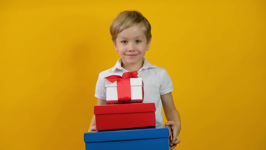 Funny happy little boy toddler smiling with gifts on yellow background