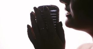 Professional singer is performing a song on concert. Woman is singing in microphone on white background, closeup lips side view. Performance on musical concert on event or party.