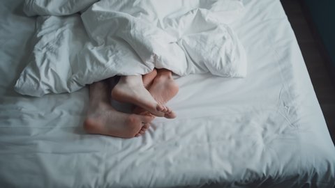 Married young couple petting in bed. Only feet in frame. Man and woman having intimate moment in bedroom under blanket. Concept of healthy relations between two people. Marriage, family, love, sex