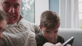 Grandfather Playing Video Game With Grandchildren On Mobile Phone At Home