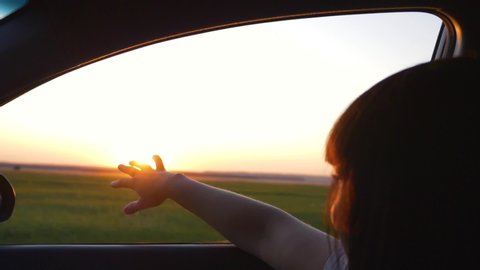 Girl traveling by car. Girl hand in the car window. Sunset in the car window. Girl travel on the road. Silhouette of a hand at sunset. Girl travels on the road by car
