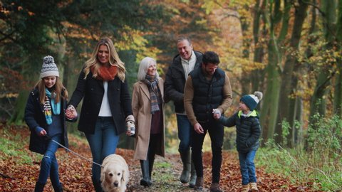 Smiling Multi-Generation Family With Dog Walking Along Path Through Autumn Countryside Together