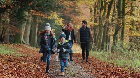Smiling Family Walking With Dog Along Path Through Autumn Countryside With Children Running Ahead