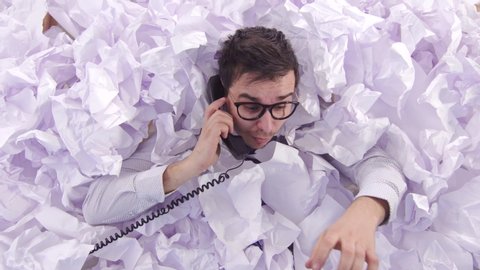 confused man office worker is talking on the phone in a large heaps of paper
