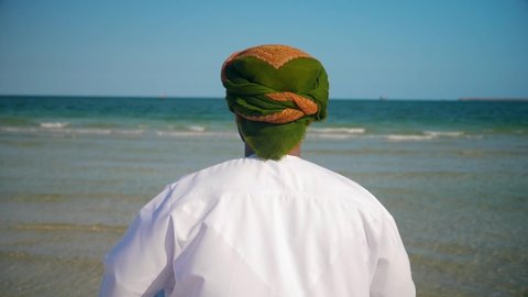 Back view of an Omani man with Oman scarf flag , wearing  omani traditional  dishdasha and  Musaar looking to the sea .