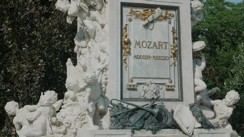 VIENNA AUSTRIA AUGUST 22 2019 Wolfgang Amadeus Mozart monument, tripod shot of Mozart memorial in city center, camera tilting upwards from Mozart memorial tablet to statue, background tree with leaves