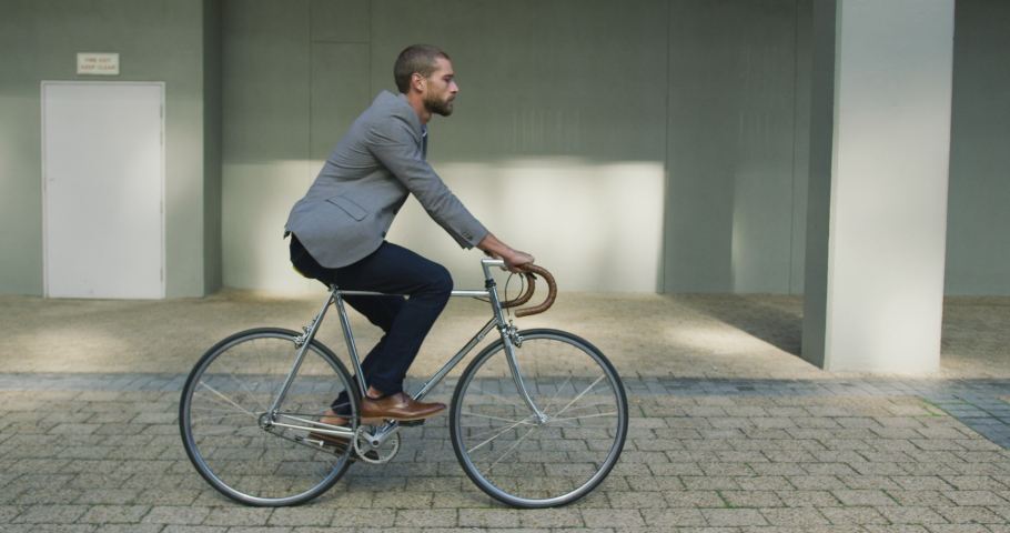 Side view of a young Caucasian businessman on the go in the city, riding a bike in the street, slow motion