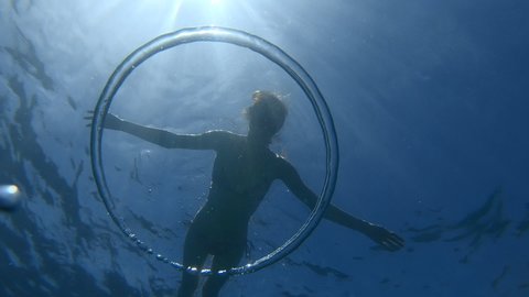 Underwater view of the ring bubble ascending to the surface with the young woman on the background