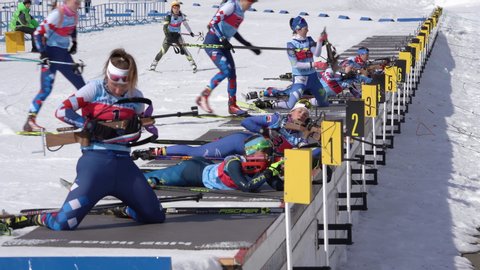 Group sportswoman biathlete aiming, rifle shooting, reloading rifle in prone position. Biathletes in shooting range stadium. Junior biathlon competitions East Cup. Kamchatka, Russia - April 14, 2019.