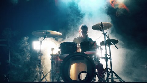 Musician is playing the drum set in the dark clouded studio. Male Drummer playing drums in smoke.