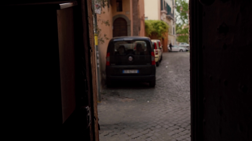 Attractive girl walks along an old city street past a camera located in a doorway. Trastevere, Rome, Italy.