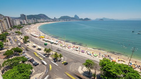 Aerial timelapse of Copacabana skyline in Rio de Janeiro city in Brazil. View of the front street traffic with car road traffic. Busy ocean beach full of activity, chairs, umbrellas, and people.  