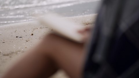 Girl reads a book on the beach by the sea on a cool windy day. Close-up of female hands holding a book.