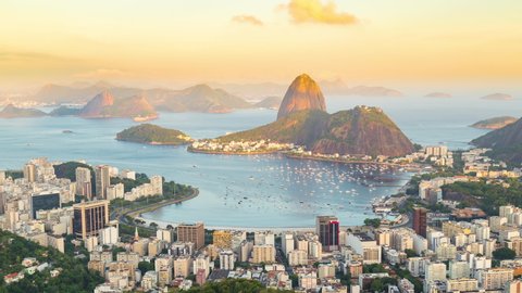 Day to night sunset timelapse of the Sugarloaf mountain in Rio de Janeiro, Brazil. View of Botafogo city buildings. Guanabara bay full of Boats and ships. Peak, rocky hills and mountain in background.