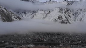 Snow mountains with low clouds. Drone video. Slow pan to the left. Fantasy view. 