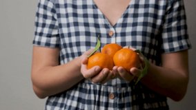 Young Caucasian woman hold fresh orange mandarins in hands. White girl in country plaid dress offers sweet tangerines fruit dessert to someone. Benefit of citrus fruits. Healthy Diet Concept.