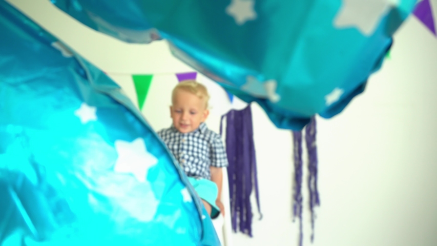 Happy two years old boy celebrating his second birthday sitting on chair with balloon. Gimbal movement shot.