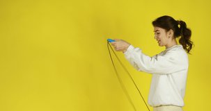 sporty girl jumping on skipping rope on yellow background