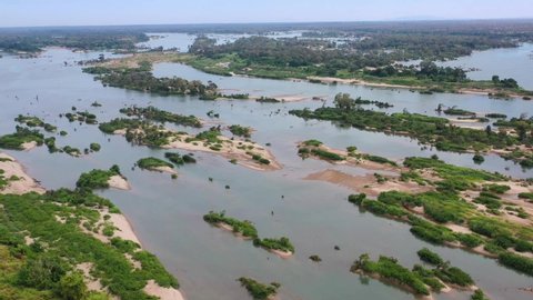 Aerial View of Mekong river affected by Spring flooding featuring Farm house, silo on dry ground, livestock, green fields, brown flood water, covered roads