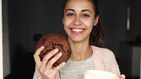 funny portrait of happy smiling woman posing with big chocolate cookie and large cup tea and quite looking at the camera. woman biting huge piece of cake and cant chew