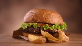 Hamburger with fries on wooden table. Hamburger on fresh buns with succulent beef and fresh salad ingredients served with French Fries in on a rustic wooden table. 4K UHD video
