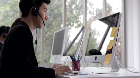 call center man wear headset working with computer and note in post it while consulting customer with online problem.support and operator service business representative concept.online marketing.