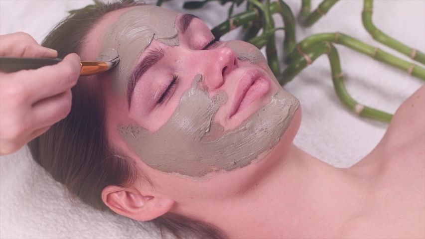 Beautiful woman applying green clay purifying mask on her face. 4K slow motion
