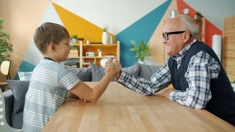 Caring grandfather is teaching boy to wrestle having fun doing sports at home, laughing grandad is winning talking to kid. Family, leisure time and lifestyle concept.