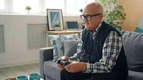 Slow motion of happy retired man enjoying video game in house playing alone winning having fun indoors at home. Elderly people and entertainment concept.