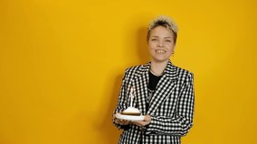 Stylish young woman celebrating birthday with a piece of pie and candle isolated over yellow background