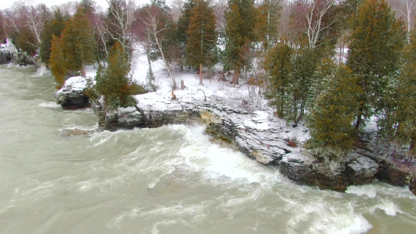Big waves driven by high winds, crash into rocky Wilderness Shoreline With Evergreen Trees. This is Cave Point in Door County, Wisconsin, in Winter.