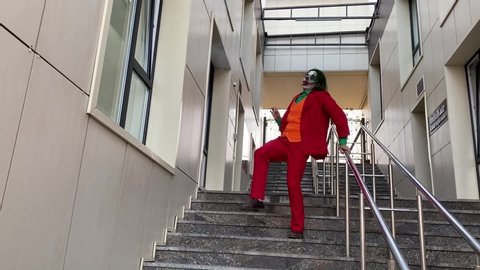 Dnipro, Ukraine - October 22, 2019: Cosplayer portrays a crazy clown Arthur Fleck from the psychological thriller "Joker" and dances against the background of the stairs in the building.