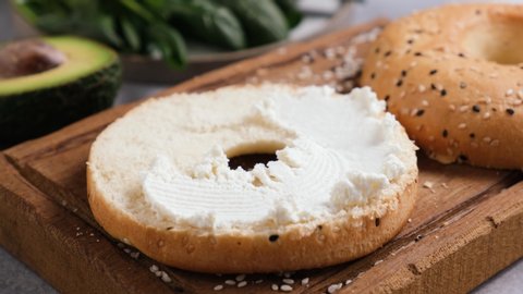 Spreading cream cheese on sesame bagel. Female hands making healthy delicious bagel and cheese toast. Footage 4K resolution