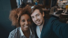 POV shot of multiracial young couple making video call sitting in modern cafe on date. African girl and caucasian guy talking on video call and waving hands. Cute couple making selfie