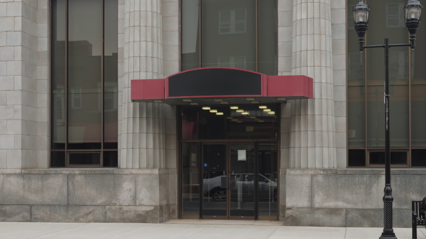 A daytime close up view of the entrance to a large bank on the main street of a small town.  	Blank sign on marquee for customization. 