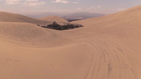 Sandy desert oasis lake. DRONE. Water in middle of hot sand desert. Romantic, holiday, couple, honeymoon, scenic shot, with sand and footprints. Tourism shot in Huacachina, Peru. Epic, dramatic shot.