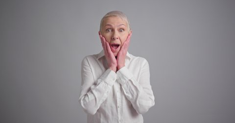 Portrait of a surprised elderly woman standing on gray background and said WOW
