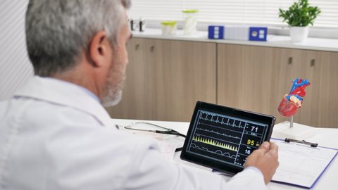 doctor watching electrocardiogram ecg data on tablet at his desk in medical office 4k