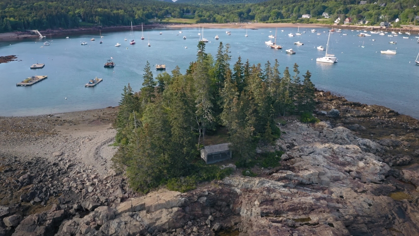 Aerial: Flying over a small island with pine trees and boats moored in the harbor. Seal Harbor, Mt Desert Island, Maine, USA 