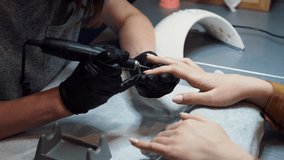 Close-up professional beautician hands working with electric drill file on client fingernails. Procedure applying artificial fingernails. Hands manicurist with tool. Manicurist gloves removes cuticle