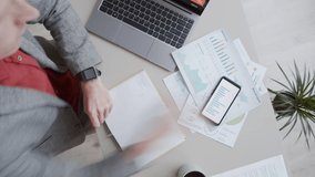 Timelapse top shot of male financial analyst sitting at desk in office, writing in notebook, using smartphone, analyzing diagrams and graphs and typing on laptop with forex trading application - Powered by Shutterstock - Get 15% off with code: PIKWIZARD15