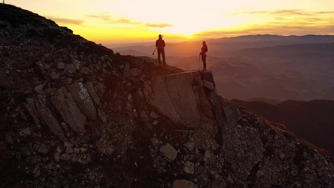 Aerial 4k drone clip with couple of hikers watching a beautiful sunset on top of Bucegi mountain ridge, during magical golden hour light in autumn season, in Romania